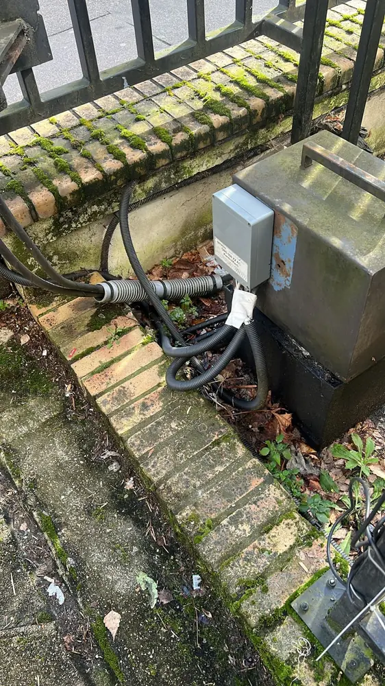 Armoire de commande d’un portail au pied d’une clôture, câbles raccordés