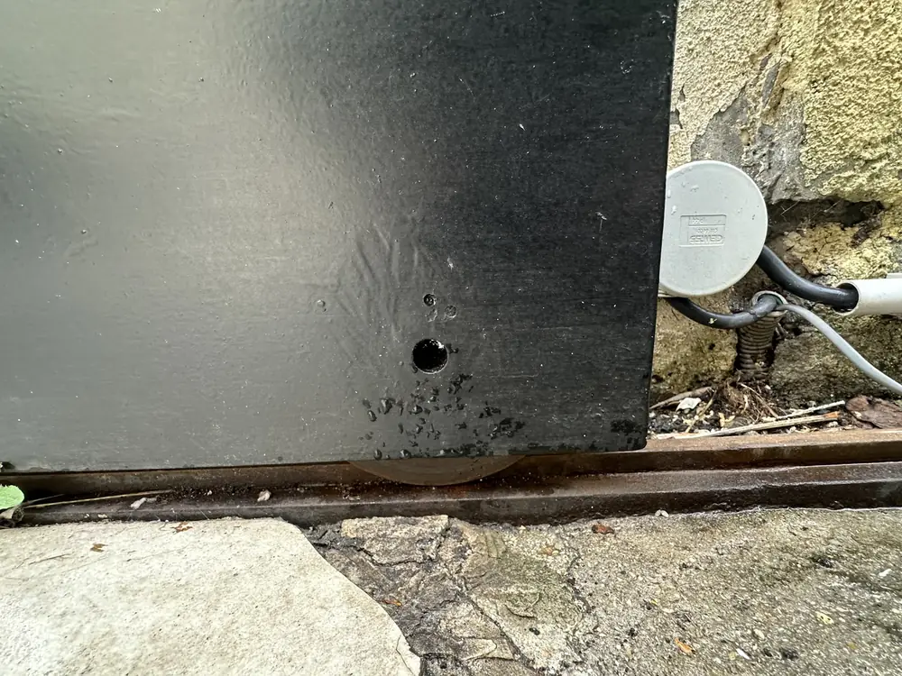 Bas d’un portail coulissant et son rail encombré, à nettoyer lors de l’entretien
