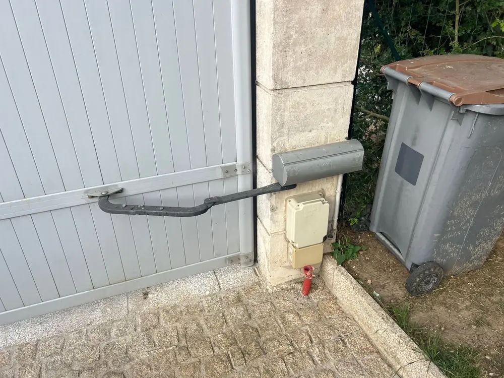 Bras articulé d’une motorisation sur un portail battant blanc, armoire de commande au pilier