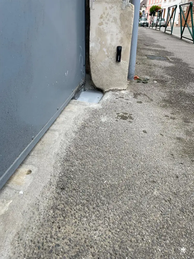 Portail coulissant gris le long d’un trottoir, seuil et guide au sol