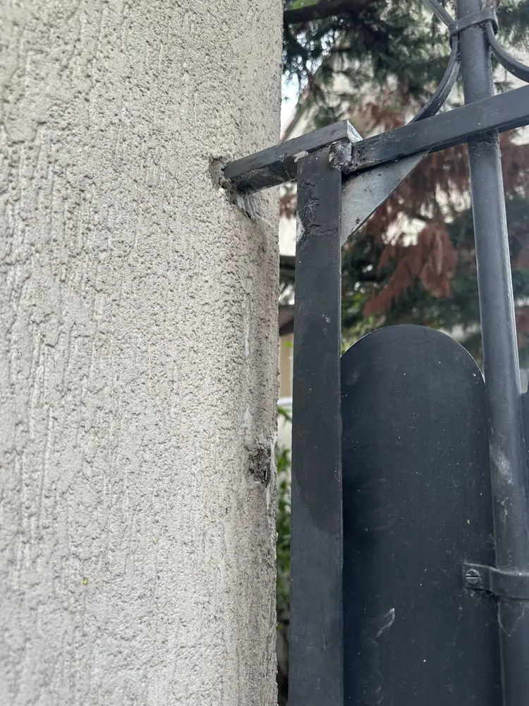 Gond d’un portillon métallique noir scellé dans un pilier crépi