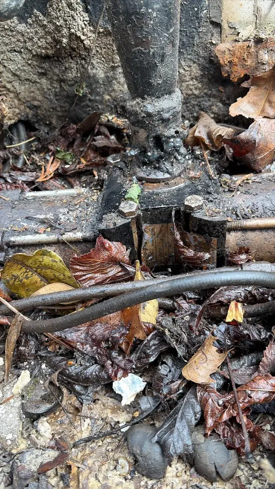 Pivot bas d’un portail battant noyé dans les feuilles et la boue, à dégager et graisser