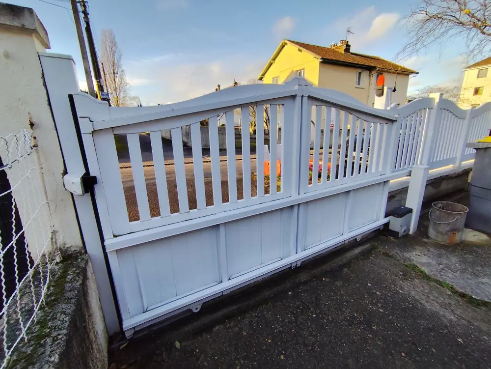 Portail coulissant blanc d’un pavillon sur son rail au sol, motorisation à droite : la longueur de refoulement se mesure le long de la clôture
