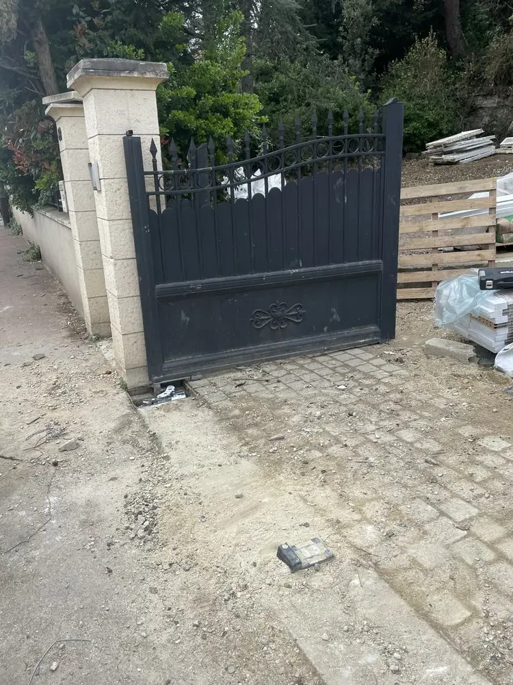 Portail battant en fer noir à barreaux ouvert sur une cour pavée