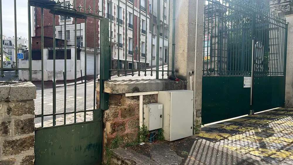 Portail et portillon verts d’un immeuble, armoire de commande au pied du pilier