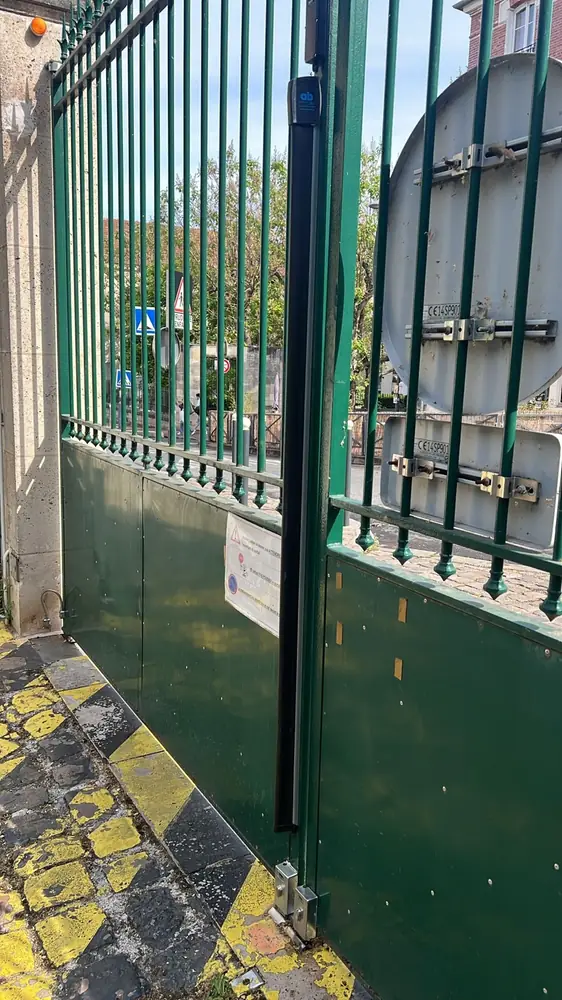 Portail vert à barreaux avec cellule de sécurité fixée sur le montant