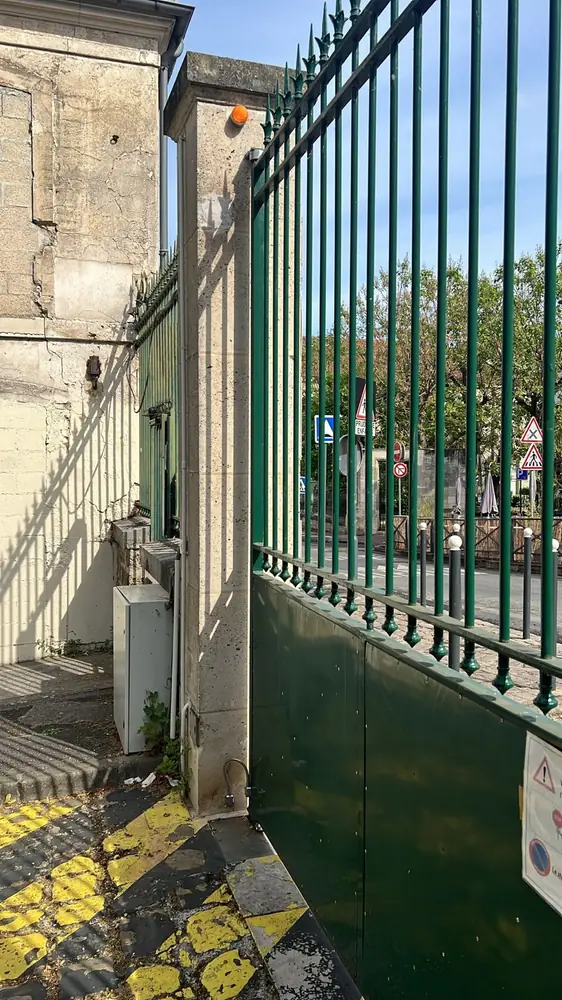 Portail battant vert à barreaux sur mur de pierre, entrée d’établissement