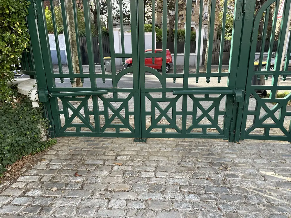 Portail vert à motifs croisés sur une allée pavée