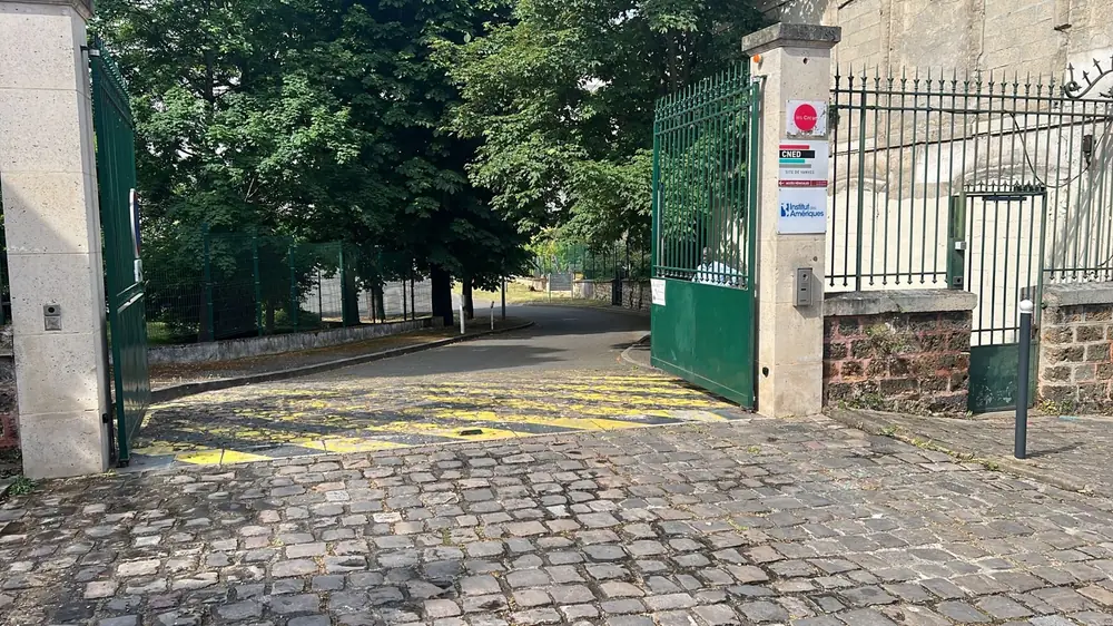 Portail battant vert ouvert sur une allée pavée, cellules et feu sur les piliers