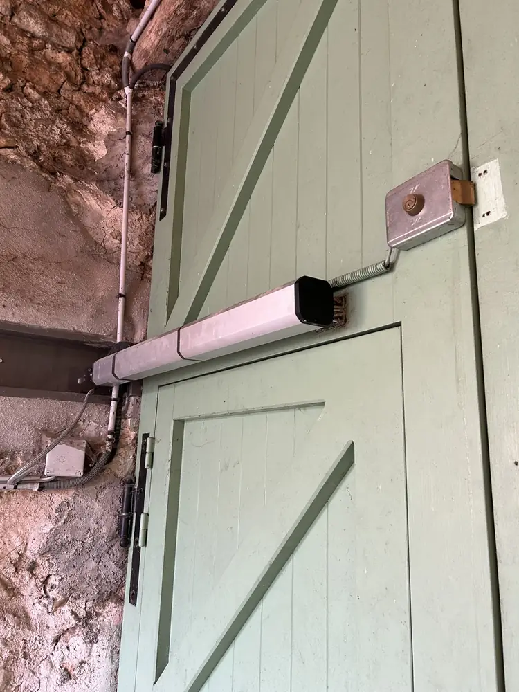 Porte de garage battante en bois vert, vérin de motorisation posé