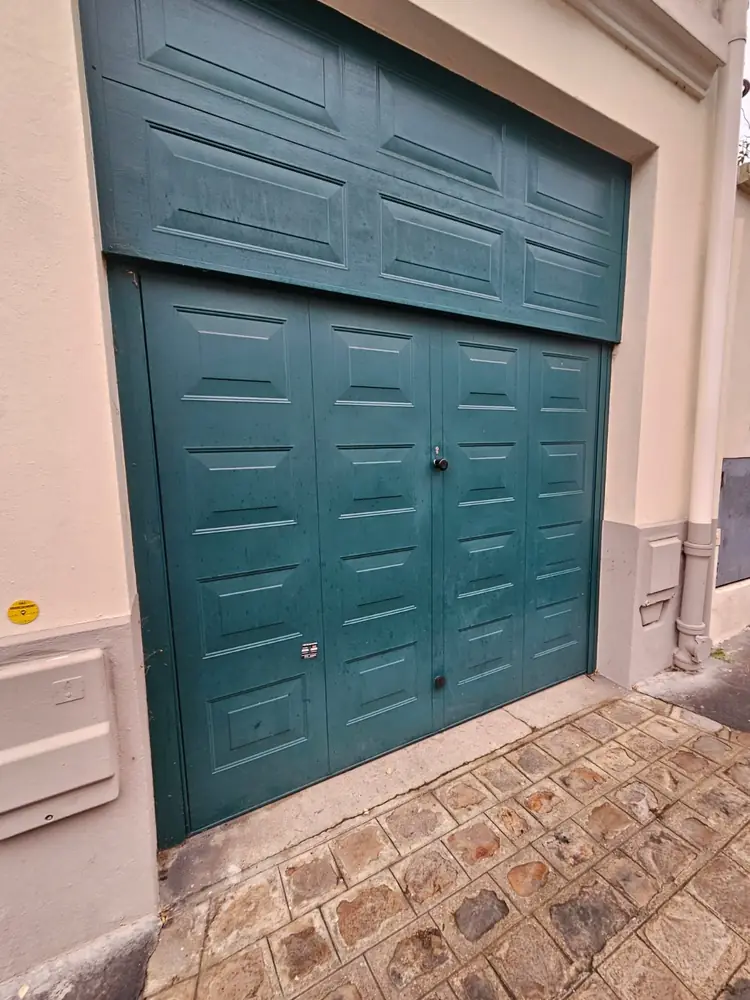 Porte de garage à panneaux verte sur une cour pavée