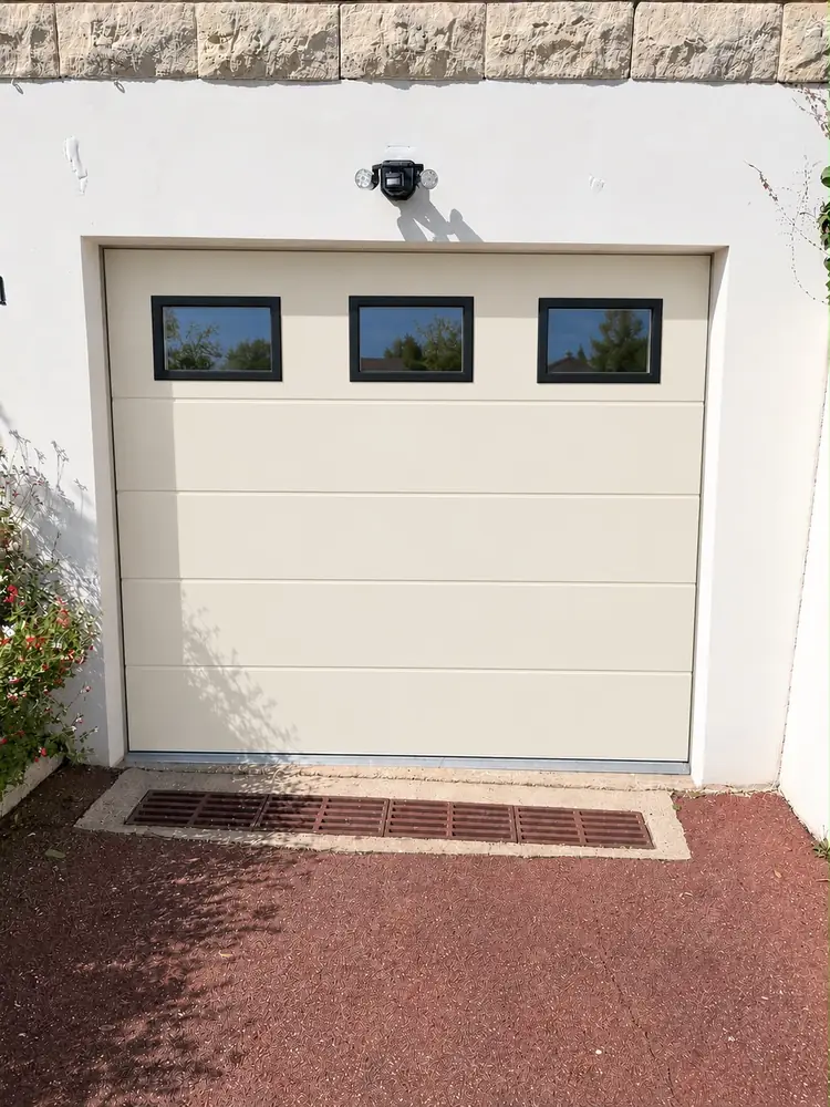 Porte de garage sectionnelle blanche à trois hublots sur la façade d’un pavillon