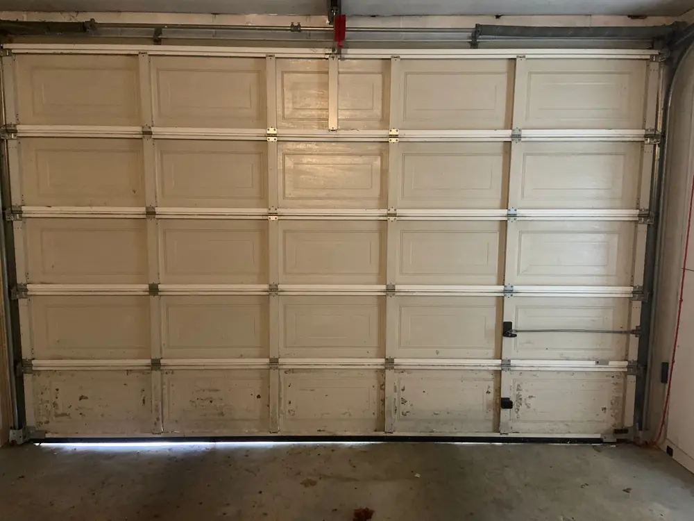 Porte de garage sectionnelle beige à caissons vue de l’intérieur, rails et charnières
