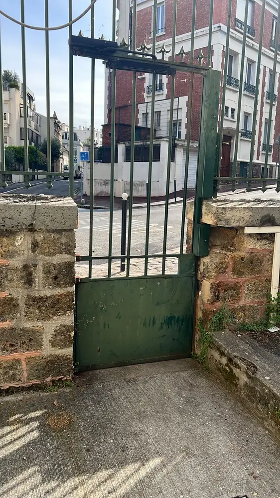 Portillon vert en tôle sur mur de brique, devant un bâtiment