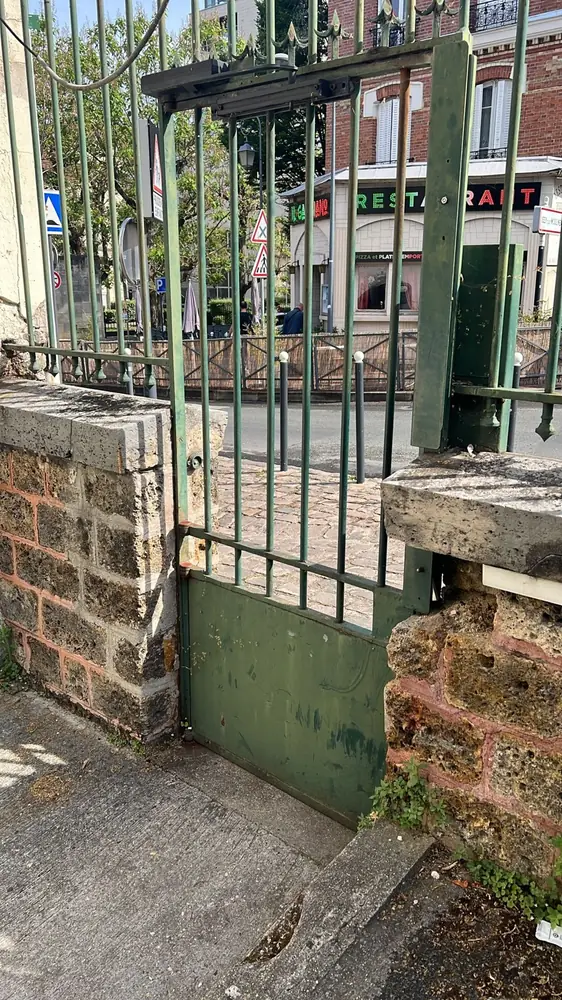 Portillon vert sur mur de brique, ouvert sur la rue