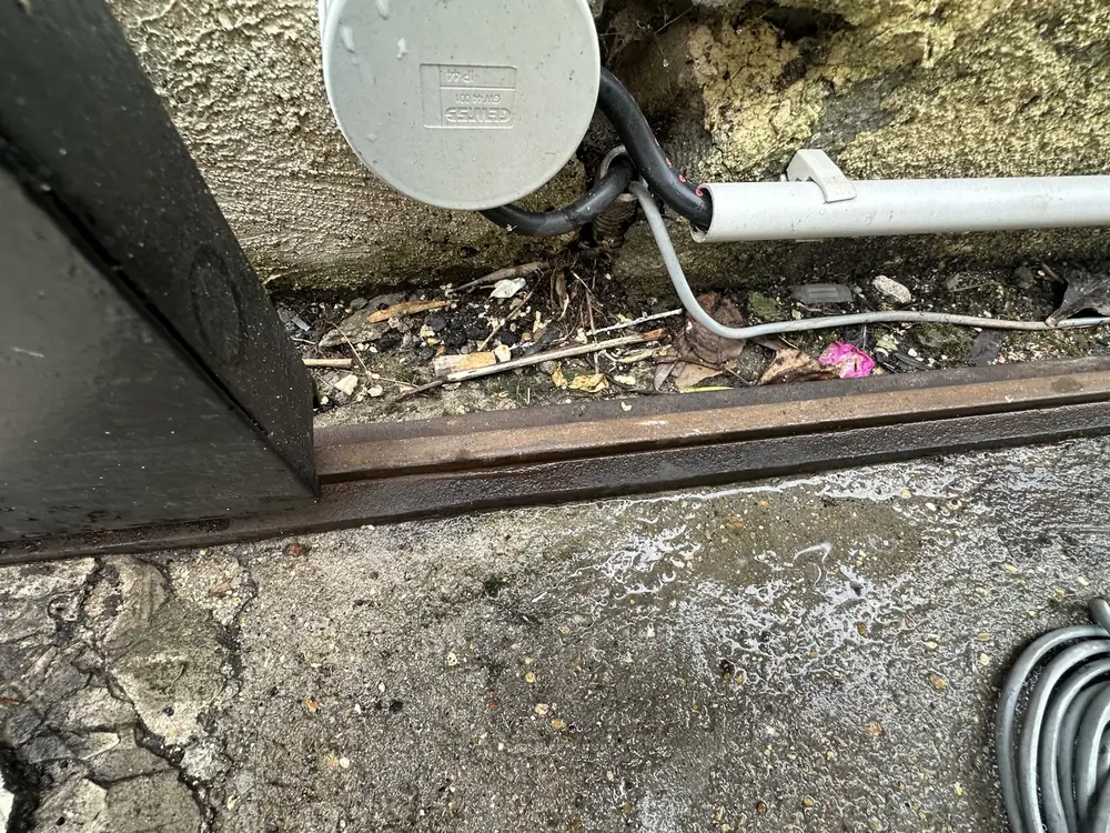 Rail au sol d’un portail coulissant encombré de feuilles et de câbles, à nettoyer avant réglage