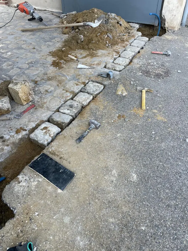 Tranchée ouverte dans une allée pavée pour le passage des câbles d’un portail