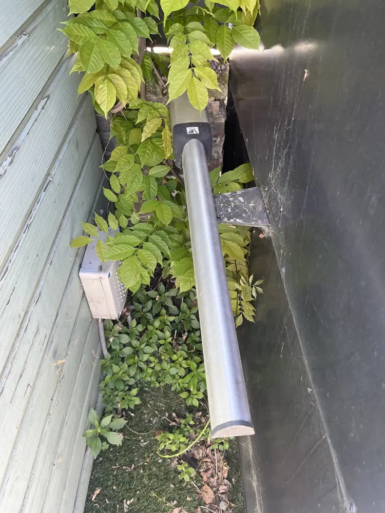 Vérin de portail battant fixé contre un mur, dans la glycine
