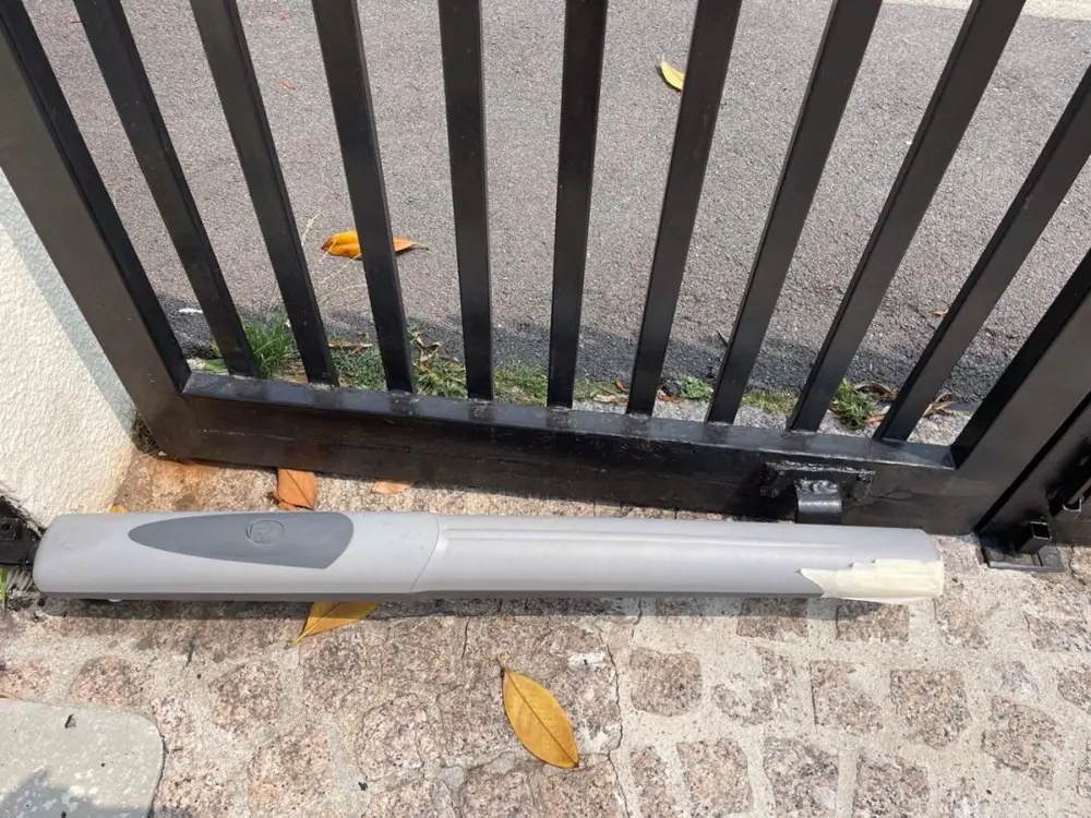 Vérin électromécanique au sol devant un portail battant noir à barreaux
