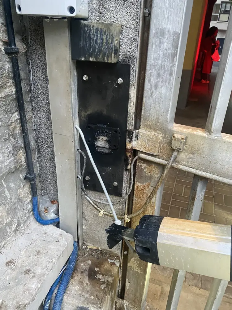 Vérin et câblage au pied du pilier d’un portail à barreaux