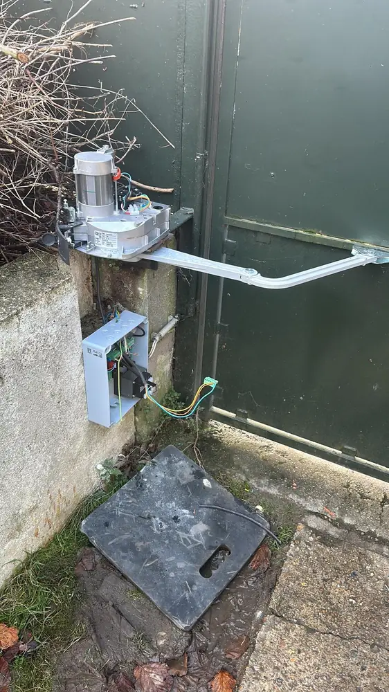 Vérin posé sur un portail battant vert, boîtier de commande sur le mur